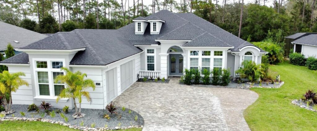 Aerial view of clean white Florida home with paver driveway and palm trees