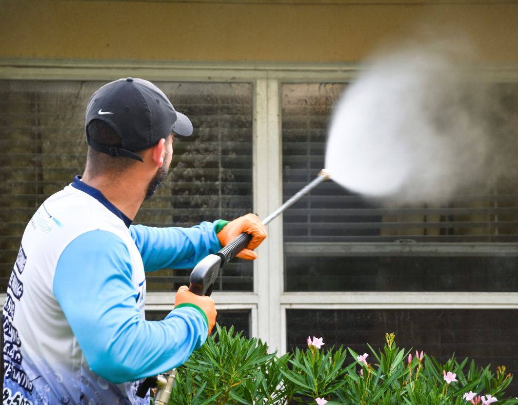 Technician pressure washing dirty windows on stucco building exterior