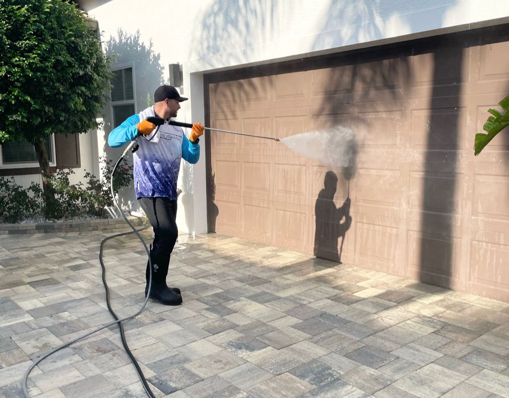 Technician pressure washing a garage door on a paver driveway