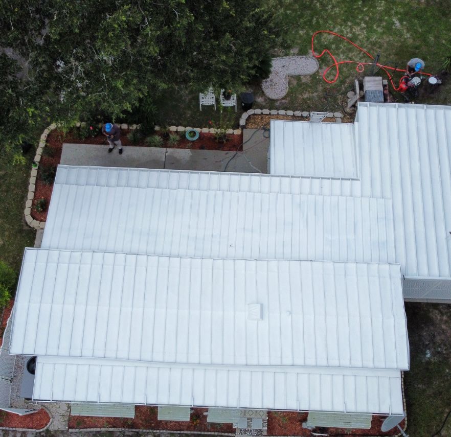 Technician applying white elastomeric coating to flat metal roof in Florida - aerial view