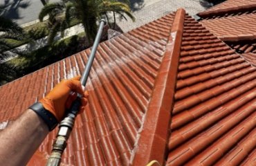 Gloved hand with pressure washing wand cleaning terracotta roof tile in Florida