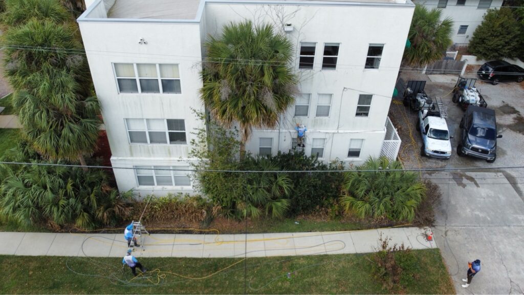Crew pressure washing a large white commercial building with palm trees in Central Florida